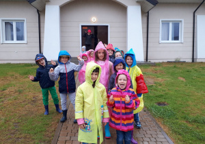 Dzieci stoją w ubraniach przeciwdeszczowych przed domkiem.
